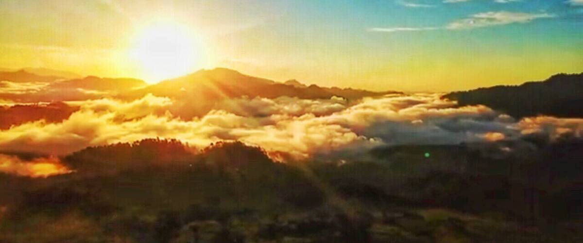 A sunrise over a mountainous landscape with clouds below the peaks.