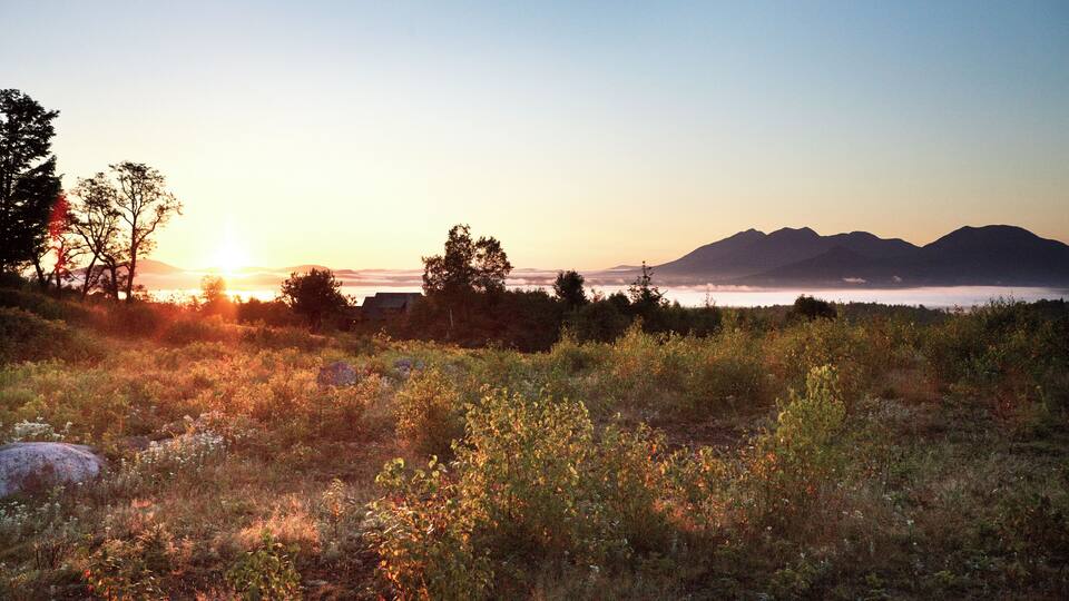 A sunset over a mountainous landscape with trees and a field.