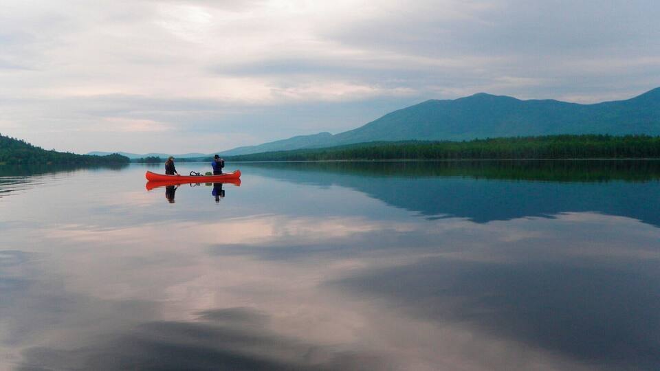 A calm lake with a red canoe and two people paddling, surrounded by mountains and dense forests.