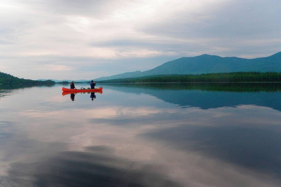 A calm lake with a red canoe and two people paddling, surrounded by mountains and dense forests.