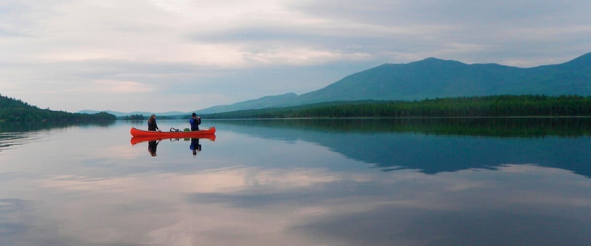 A calm lake with a red canoe and two people paddling, surrounded by mountains and dense forests.