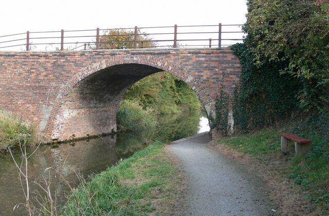 A brick bridge over a narrow waterway with a bench on the right.