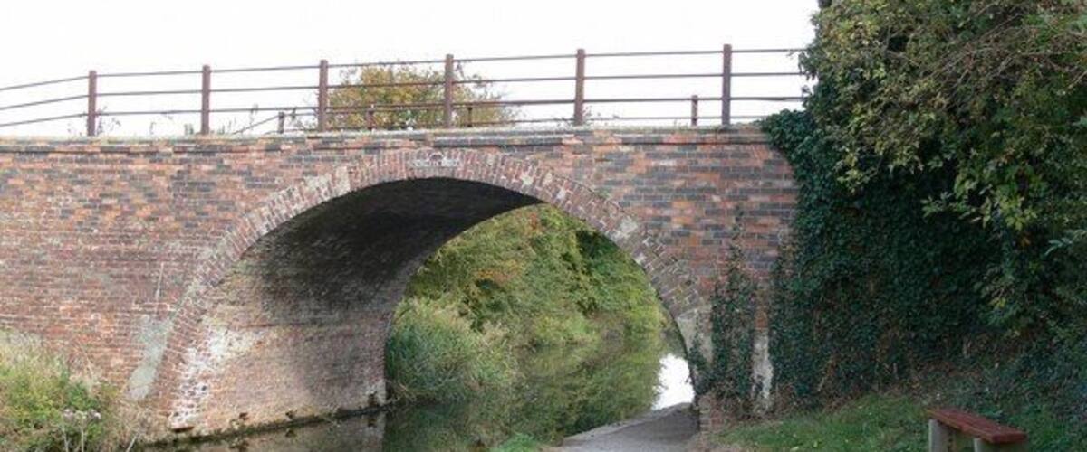 A brick bridge over a narrow waterway with a bench on the right.