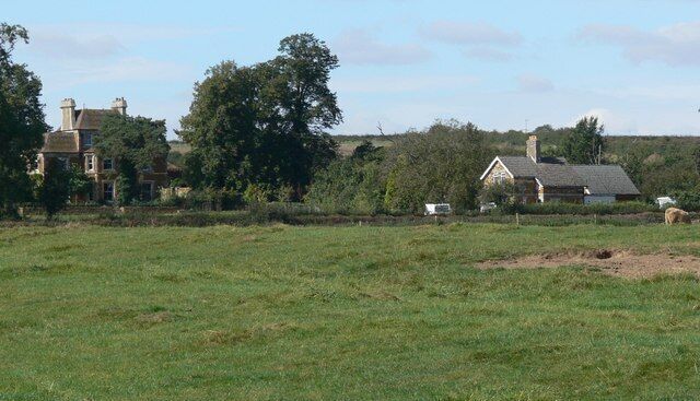 A rural landscape with a large field, a farmhouse, and a large tree.