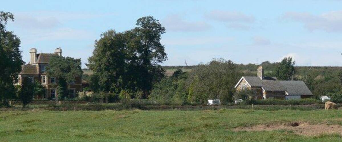 A rural landscape with a large field, a farmhouse, and a large tree.