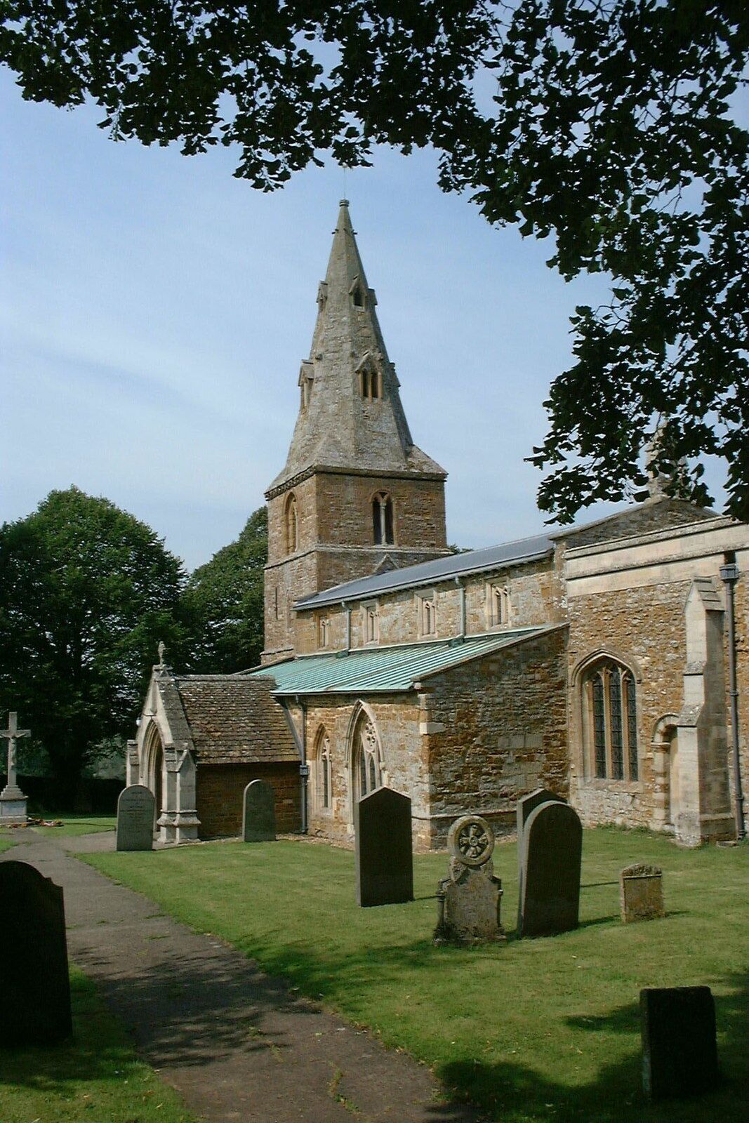 A church with a tall steeple and a green roof, surrounded by a cemetery with headstones.