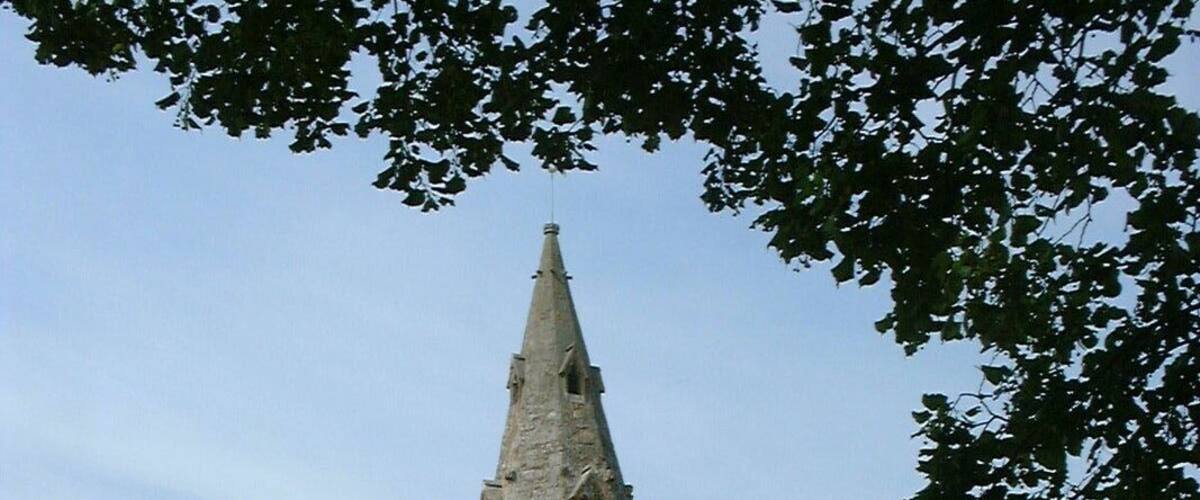 A church with a tall steeple and a green roof, surrounded by a cemetery with headstones.