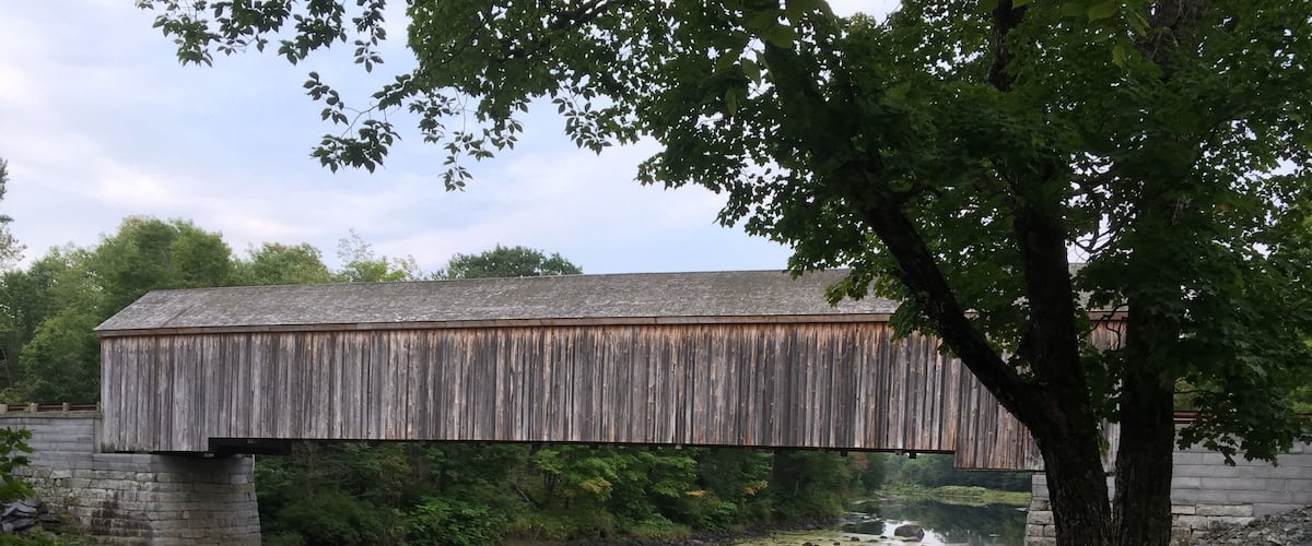 A wooden covered bridge over a river with rocks and lily pads.