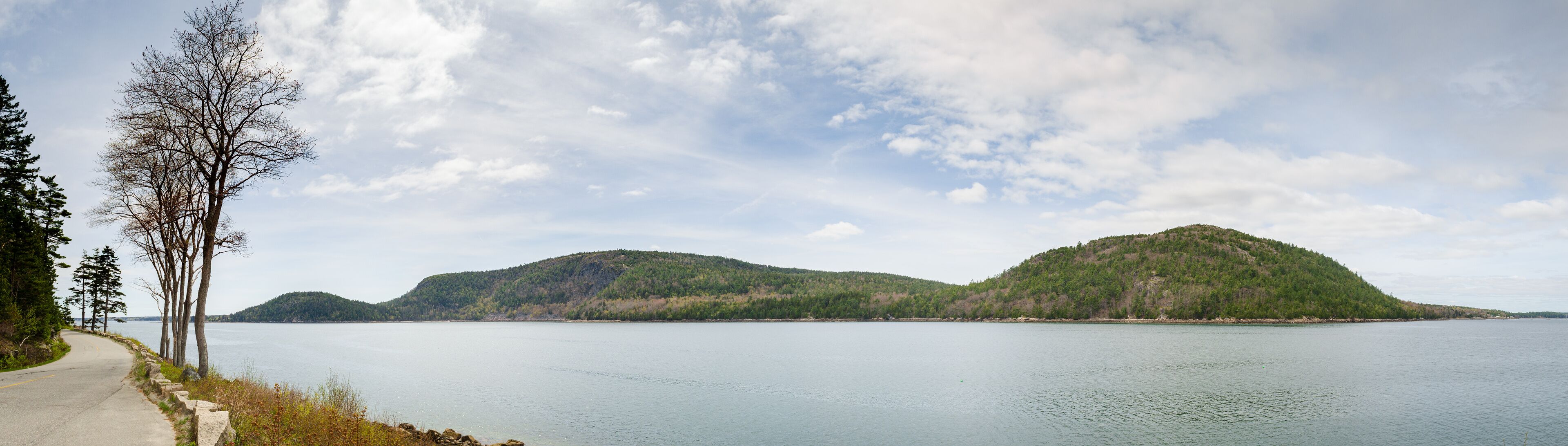 A calm lake with two hills in the background and a paved path on the left.