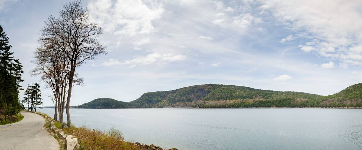 A calm lake with two hills in the background and a paved path on the left.