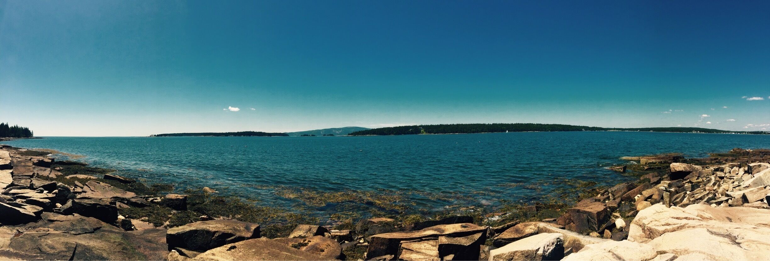 A rocky shoreline with clear blue water and distant land.