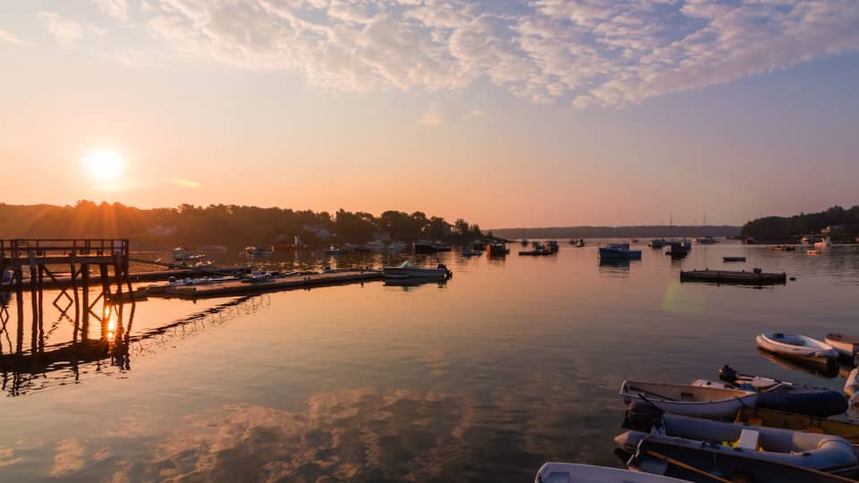 A marina at sunset with boats docked, a pier, and a calm water reflecting the sky.