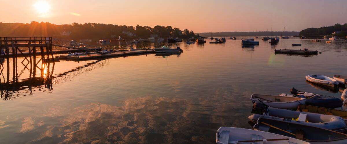 A marina at sunset with boats docked, a pier, and a calm water reflecting the sky.