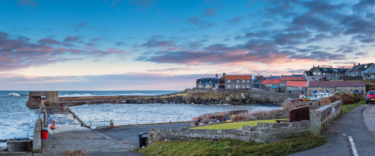 A coastal town with stone buildings, a sea wall, and a rocky shoreline.