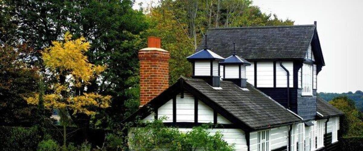 A traditional house with a black roof, white walls, and a brick chimney.