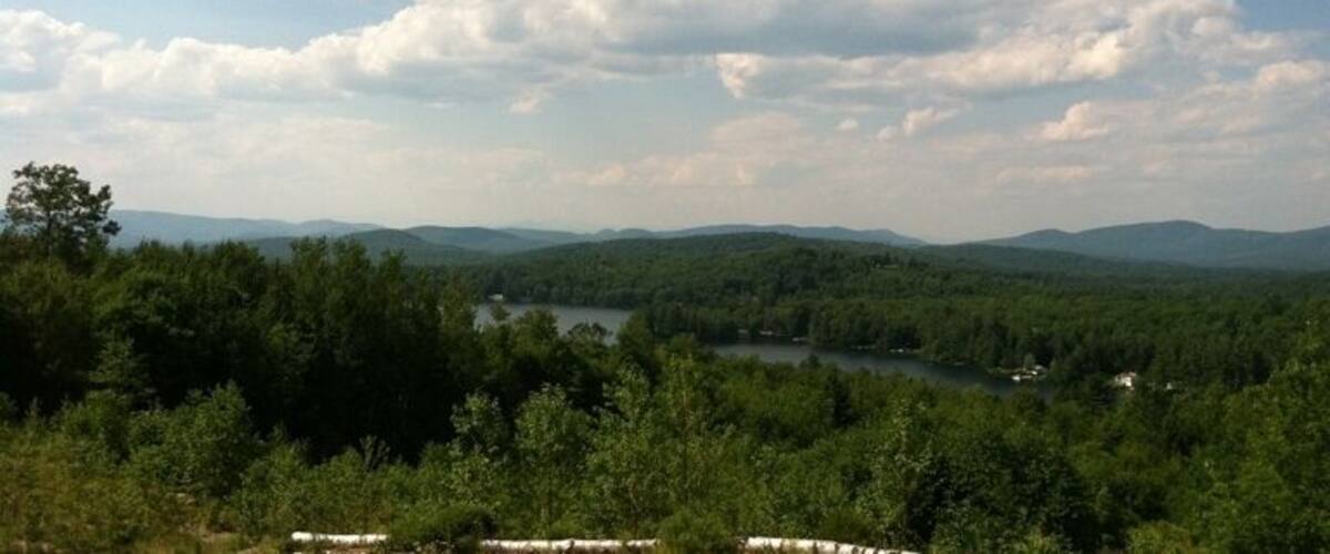 A river winding through a forested valley with distant hills under a partly cloudy sky.