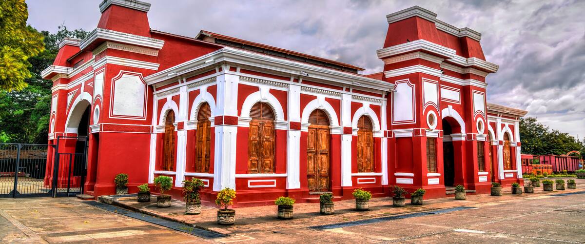 A red and white colonial-style building with arched windows and doors, surrounded by potted plants.