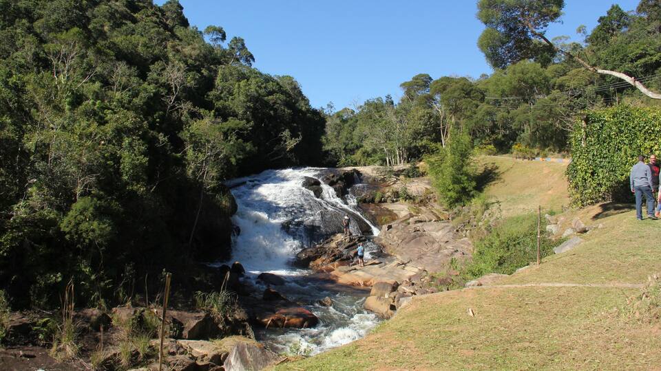 A waterfall in a forested area with a person standing on a rock near the water.
