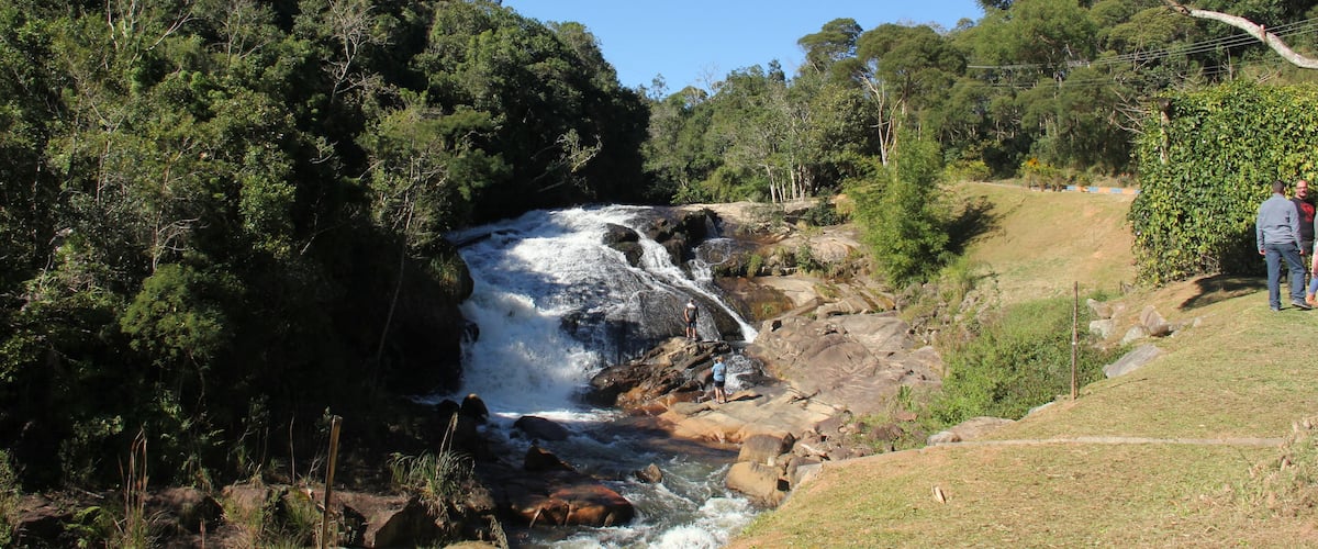 A waterfall in a forested area with a person standing on a rock near the water.