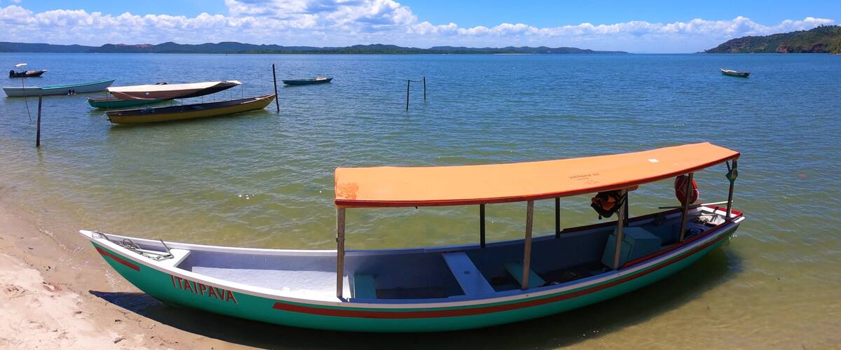 A beach with several boats, including a green and white boat with 'ITAIPAVA' written on it, anchored near the shore.