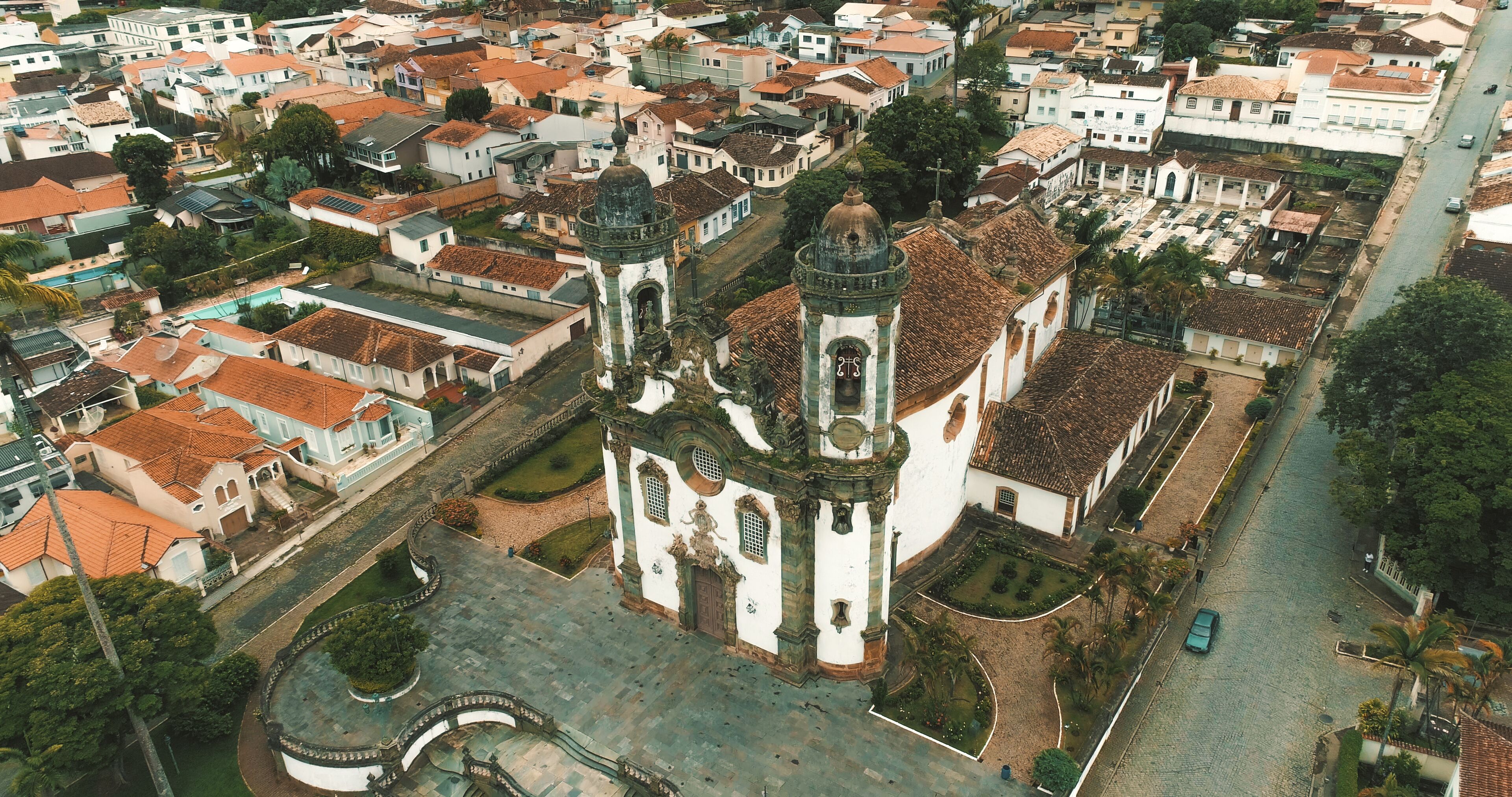 An aerial view of a historic town with a prominent church featuring a dome and bell tower, surrounded by traditional buildings and a central square.