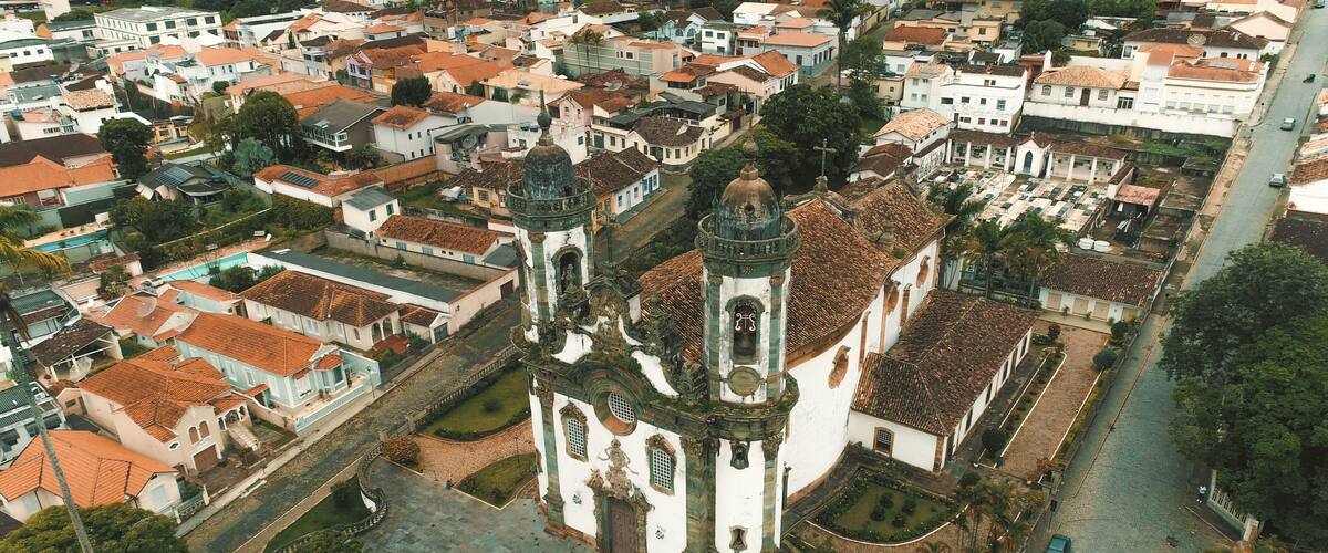An aerial view of a historic town with a prominent church featuring a dome and bell tower, surrounded by traditional buildings and a central square.