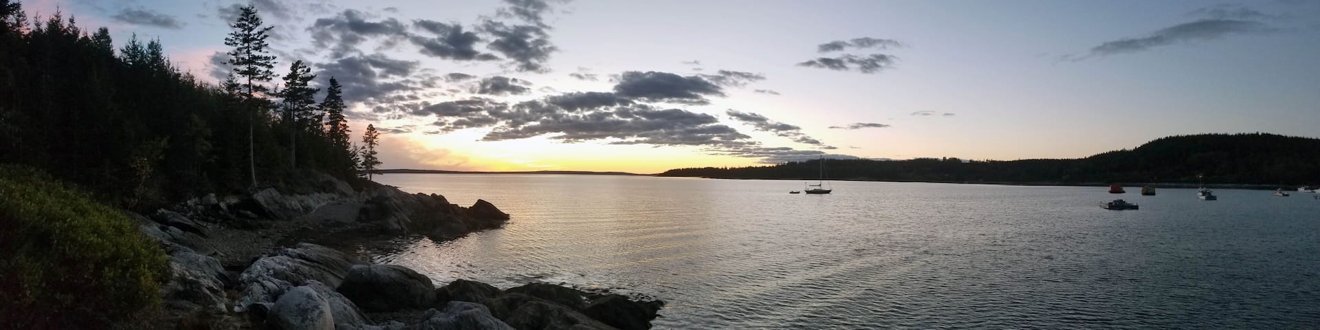 A calm lake at sunset with rocky shores and sparse vegetation.