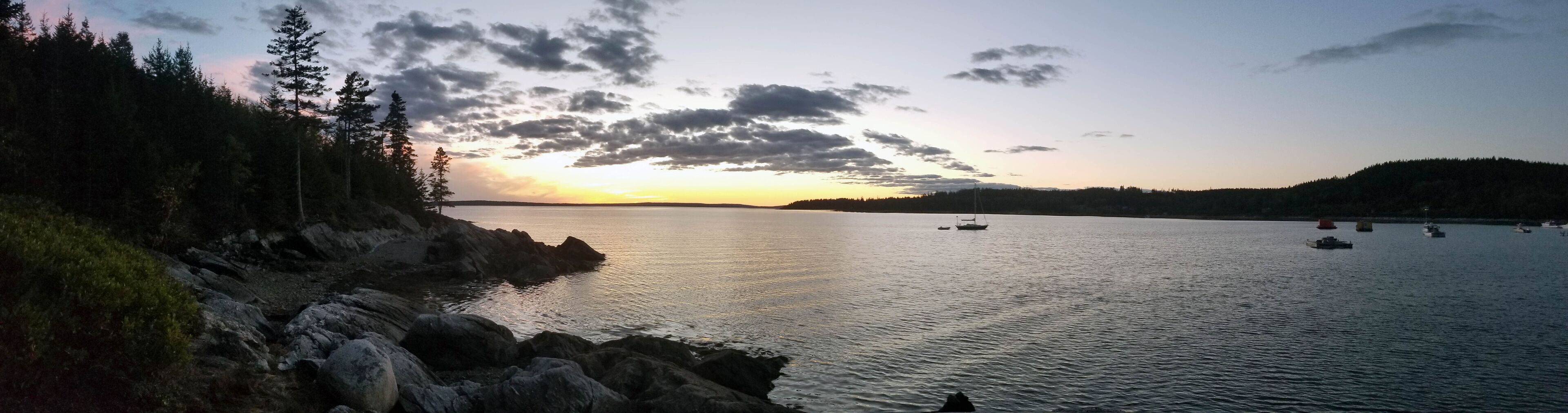 A calm lake at sunset with rocky shores and sparse vegetation.
