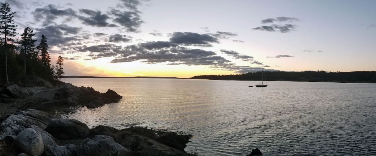 A calm lake at sunset with rocky shores and sparse vegetation.