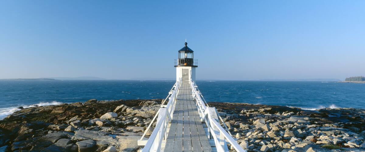 A lighthouse on a rocky pier extending into the ocean.