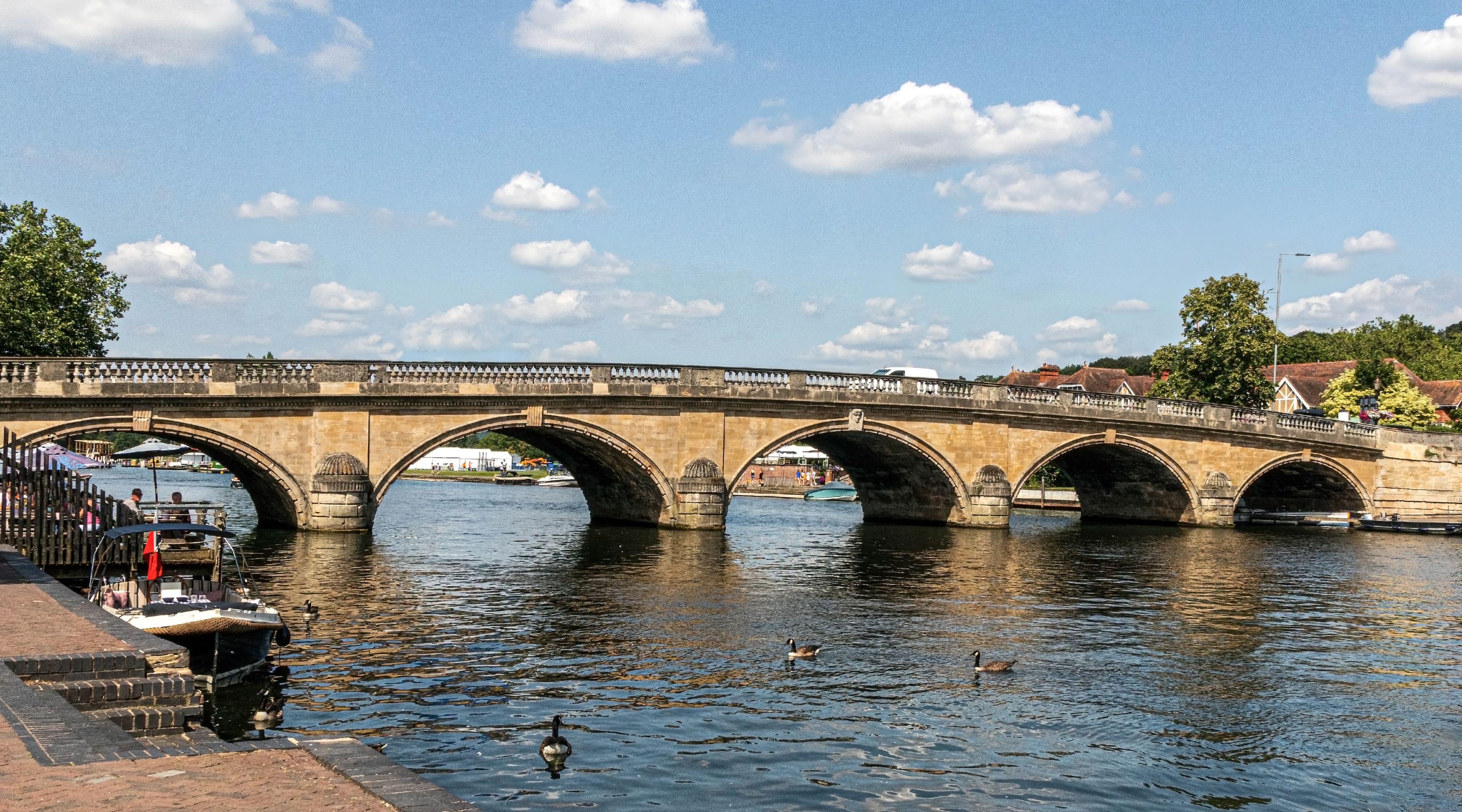 A stone bridge over a river with ducks swimming below.