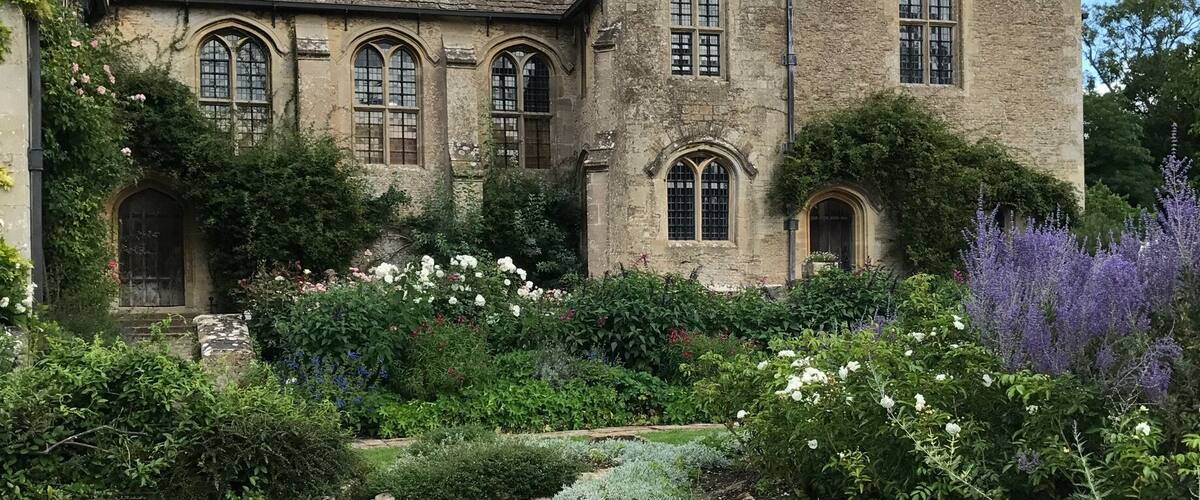 A historic stone building with arched windows and a well-maintained garden.