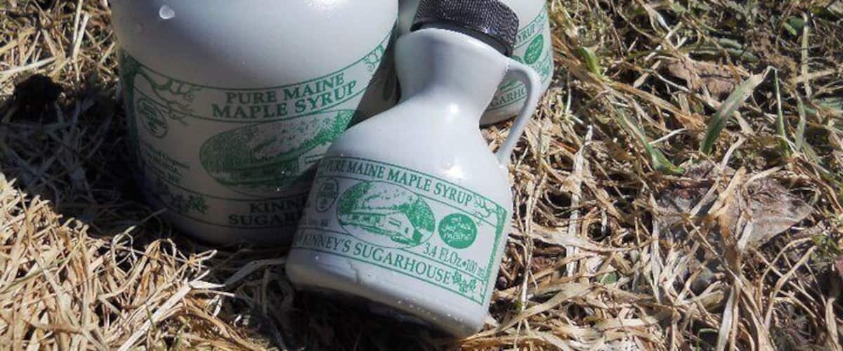 Three bottles of maple syrup and a smaller container on a grassy surface.