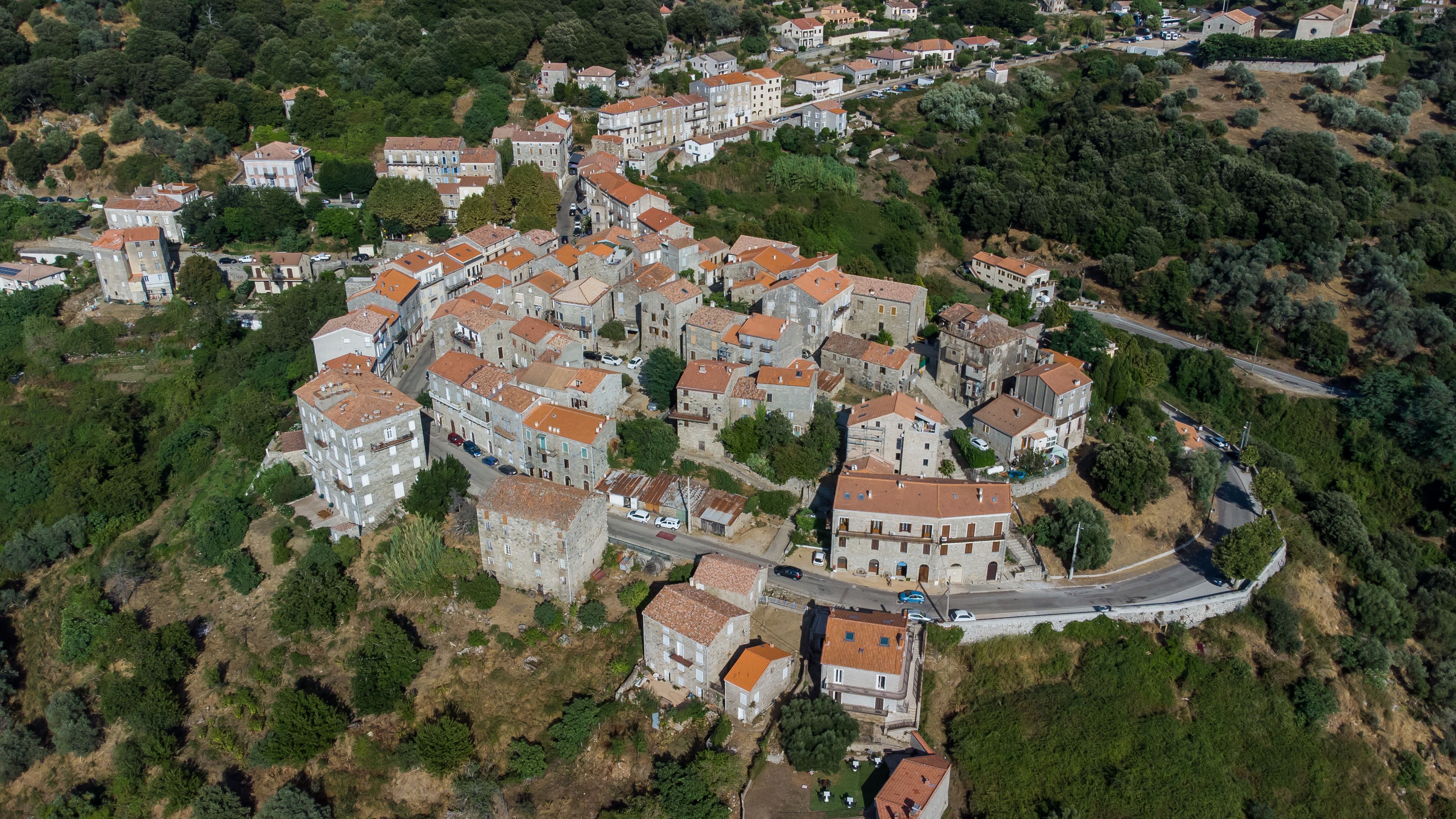 Vista aérea de uma vila densamente construída em uma encosta, com casas em terraços e uma estrada sinuosa.