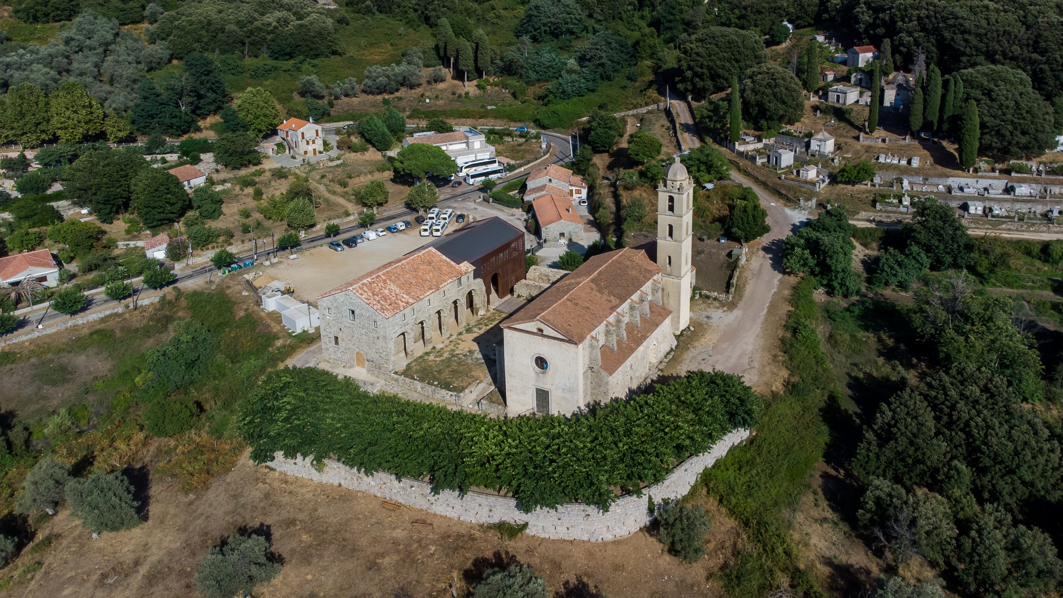 Vista aérea de uma cidade histórica com uma igreja imponente, um cemitério e áreas verdes ao redor.