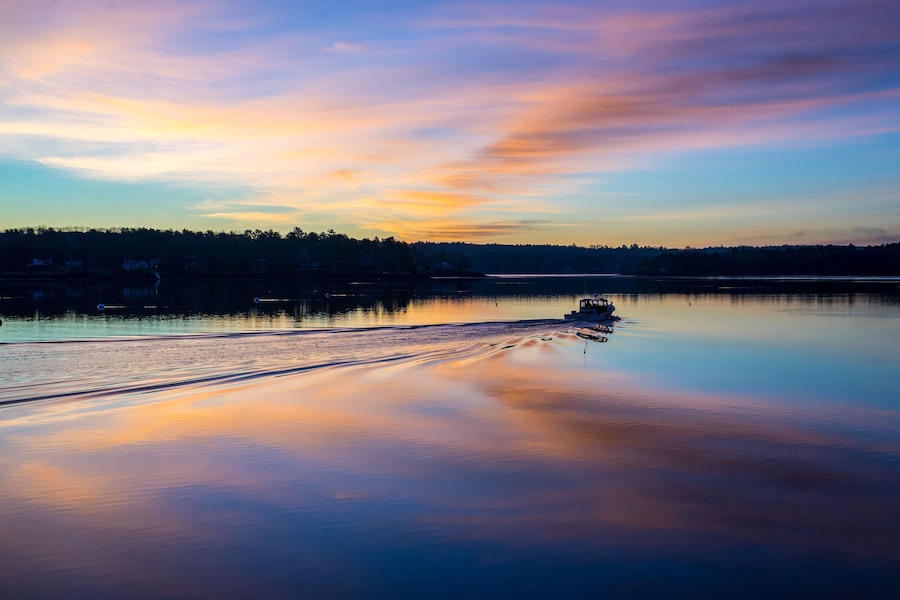 Um lago tranquilo ao pôr do sol, com um barco na água e uma floresta ao fundo.