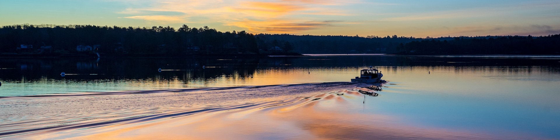 Um lago tranquilo ao pôr do sol, com um barco na água e uma floresta ao fundo.