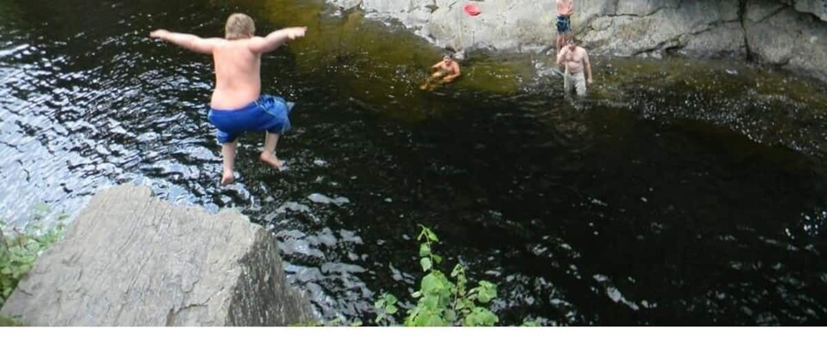A rocky riverbank with a man jumping into the water and others swimming nearby.