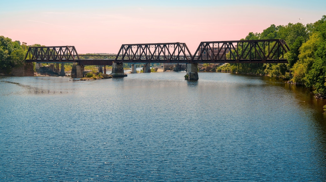 Rustic railway tracks and the historic Waterville–Winslow Railroad Bridge span the Kennebec River in Waterville, Maine, USA—a steel truss structure built around natural rock formations
