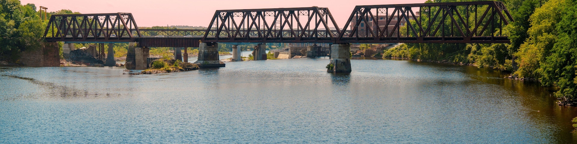 Rustic railway tracks and the historic Waterville–Winslow Railroad Bridge span the Kennebec River in Waterville, Maine, USA—a steel truss structure built around natural rock formations