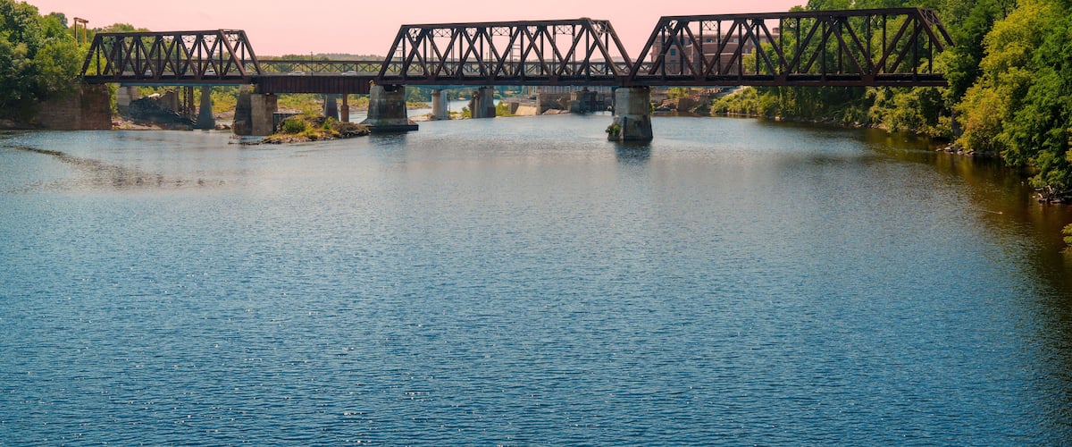 A steel bridge over a river with lush greenery on both sides.