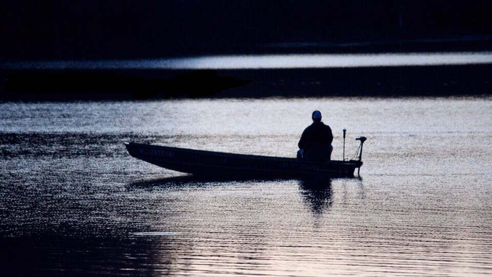A person in a small boat on a calm body of water.