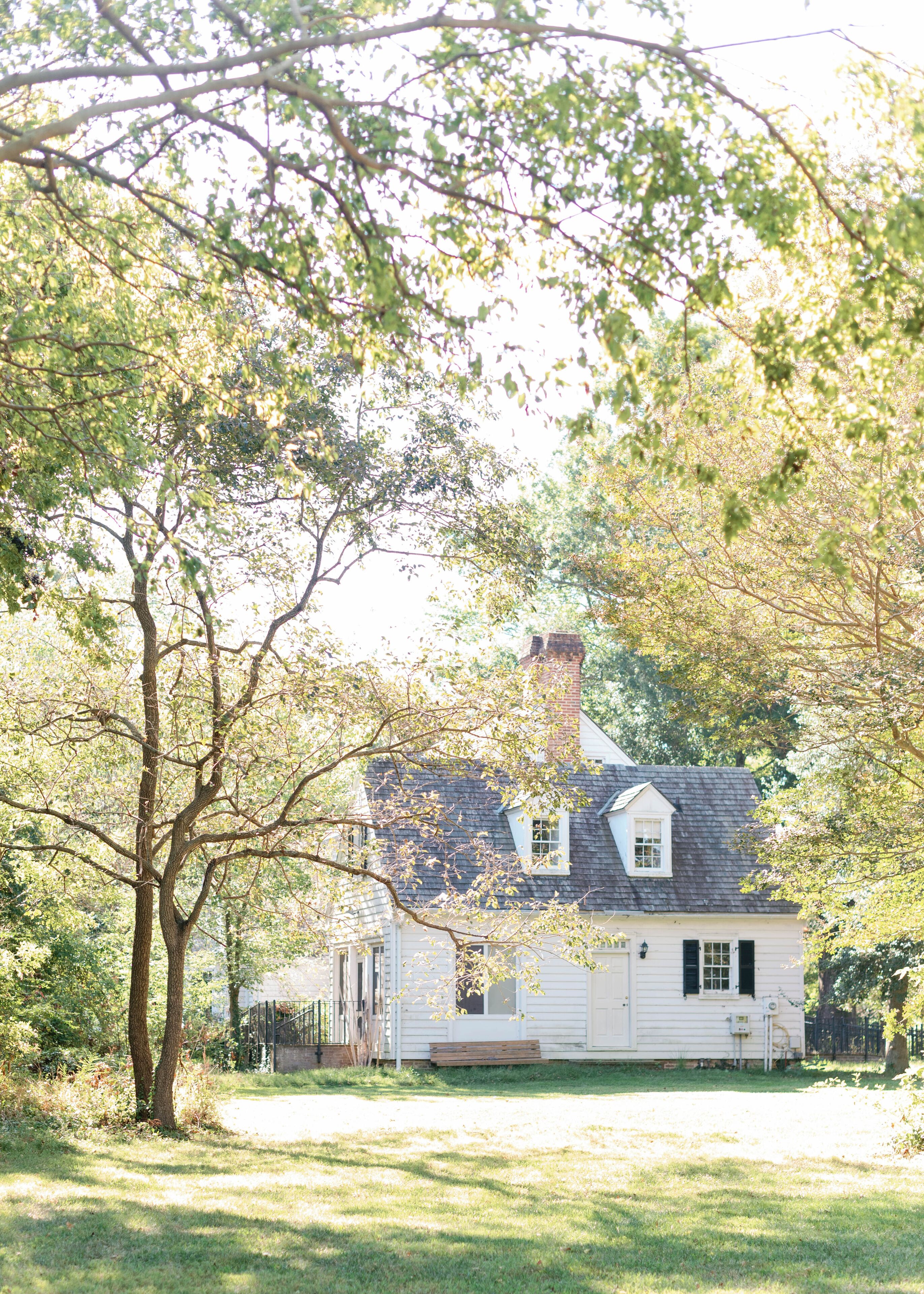 A white house with a chimney, surrounded by trees and a grassy yard.