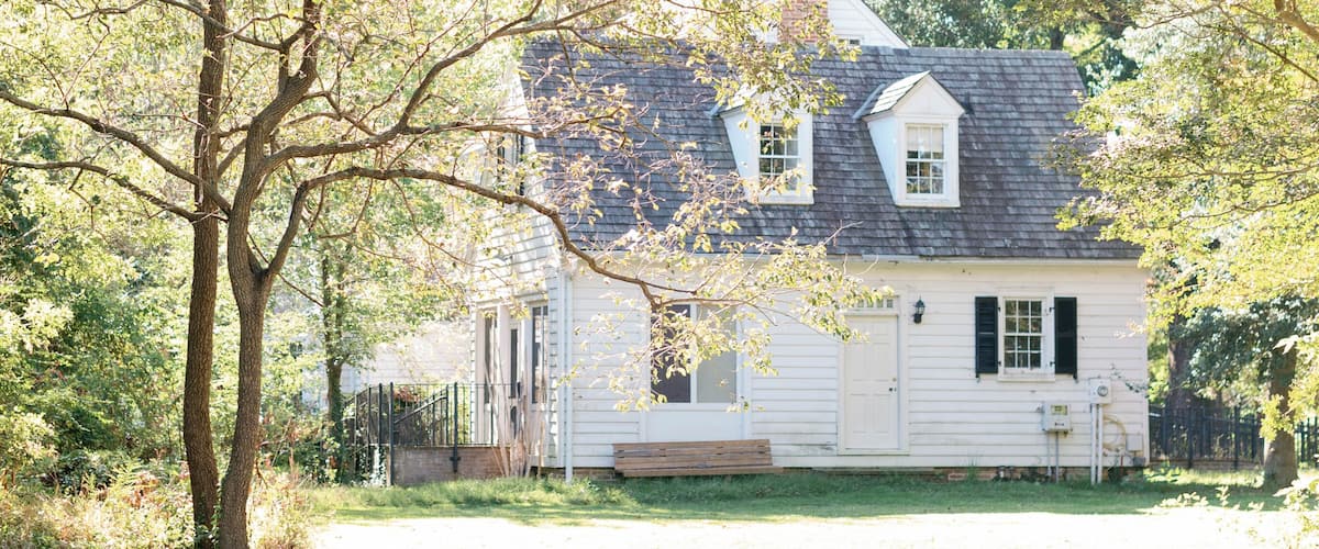 A white house with a chimney, surrounded by trees and a grassy yard.
