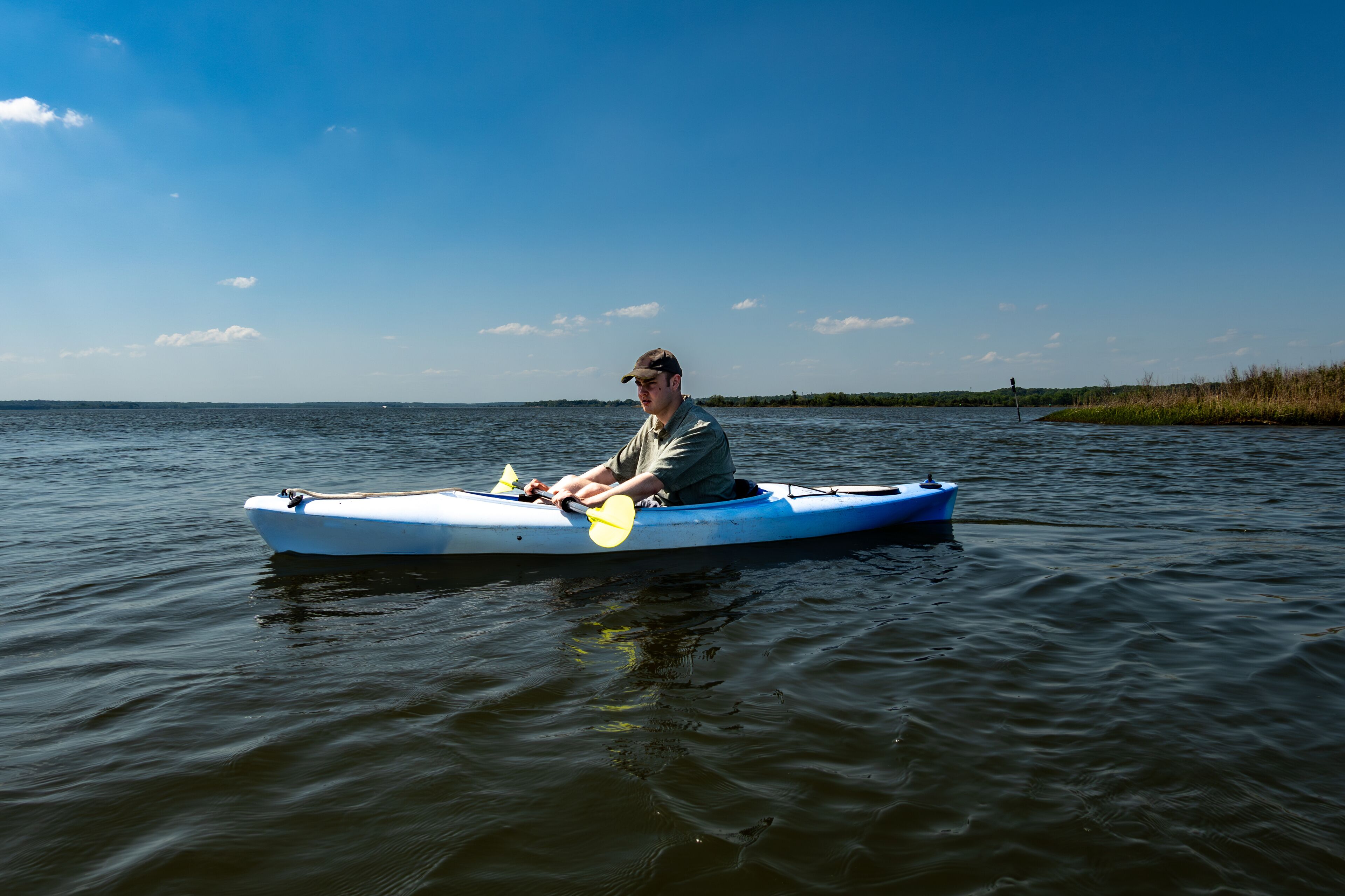 A man in a kayak on a calm body of water with a clear sky and distant shoreline.