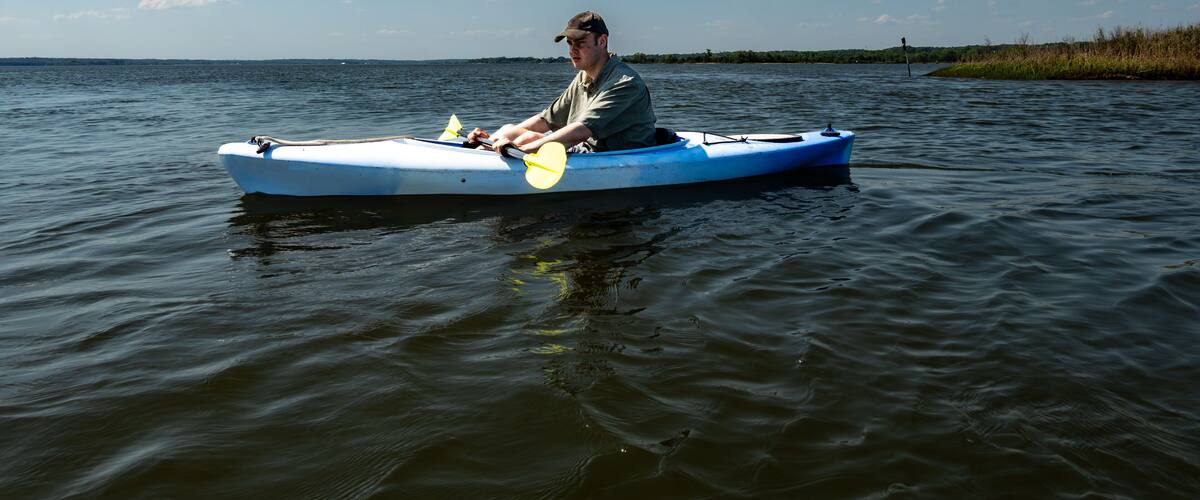 A man in a kayak on a calm body of water with a clear sky and distant shoreline.