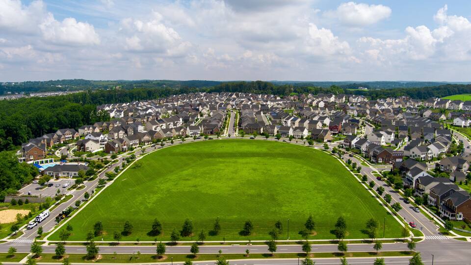 A suburban neighborhood with a large green park, houses, and roads.