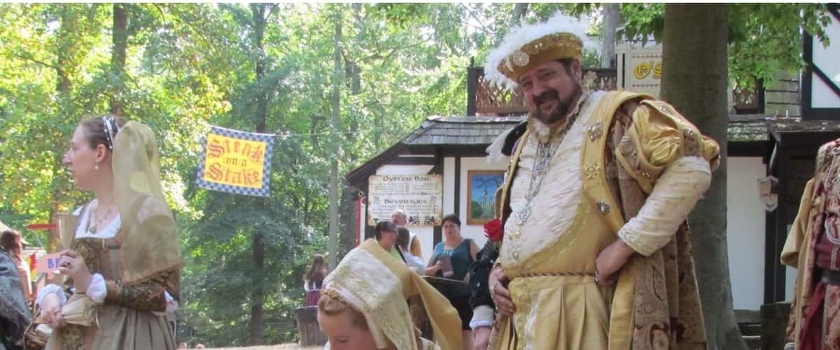 People in historical costumes at an outdoor event with signs for 'Oyster Bar' and 'Beverages'.