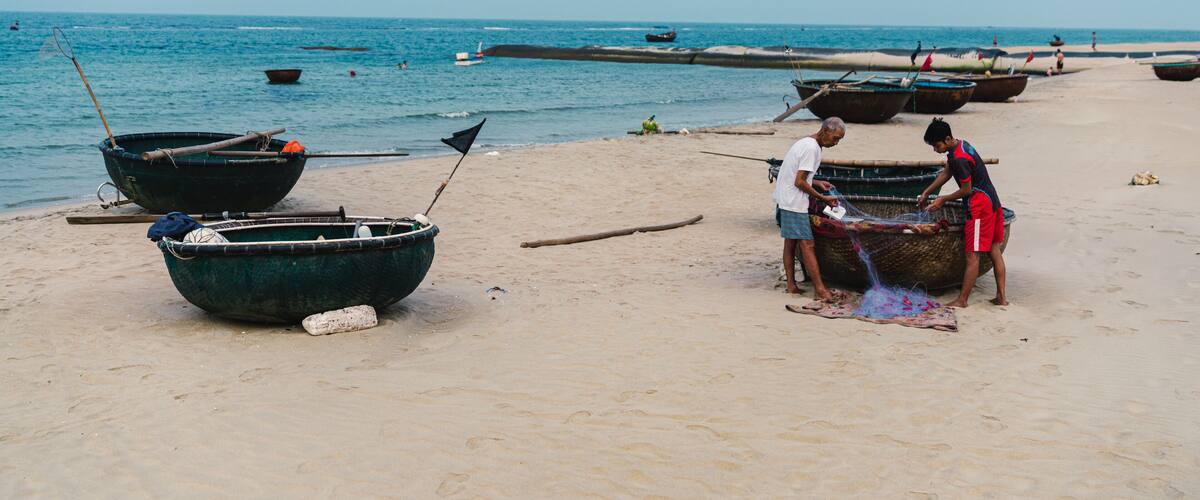 A beach with several boats and people fishing.