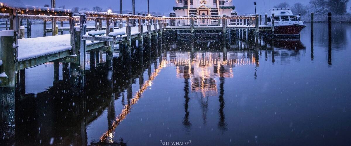A snow-covered pier with a boat docked at a dock, reflecting in calm water.